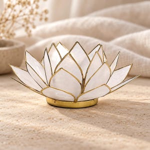 May include: A lotus flower candle holder featuring translucent white shell petals framed in thin gold metal edges. The base is a solid gold metal disc that supports the layered petal structure, creating a bowl-like shape for holding a small candle.