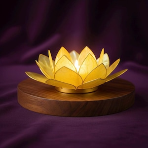 May include: A golden lotus flower candle holder with a lit candle inside, resting on a round, dark wooden base. The petals are a bright yellow, and the base is a rich brown. The background is a deep purple.
