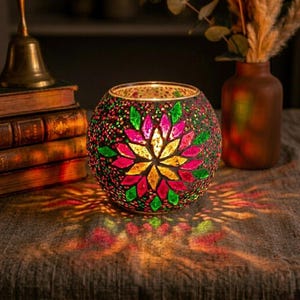 Op de afbeelding: Een ronde kandelaar van mozaïekglas met een bloemmotief in roze, geel en groen. De kandelaar staat op een tafel, met licht dat door het glas schijnt en kleurrijke patronen creëert.
