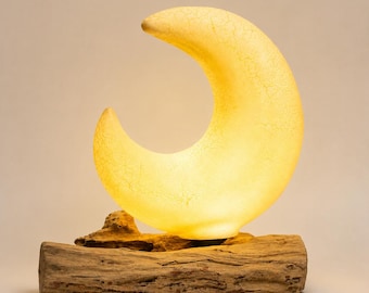 May include: A crescent moon-shaped lamp with a warm, glowing yellow light and a visible crackle texture on its surface. The lamp is mounted on a horizontal piece of natural, textured brown driftwood that serves as a sturdy base for the light.