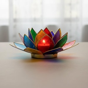 May include: A vibrant lotus flower candle holder with a lit red candle. The petals are made of stained glass in shades of blue, green, orange, and purple. The candle holder has a gold-coloured metal base, creating a striking display.