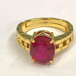 May include: A gold ring featuring a large, oval, deep red gemstone. The ring has a textured band with a brick-like design. The gemstone is secured by four prongs. The ring is likely made of gold.