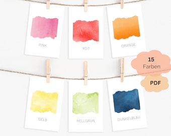 May include: A collection of color swatches, each displaying a different watercolor hue. The cards are suspended by clothespins on a string. Colors include pink, red, orange, yellow, light green, and dark blue. Text on the cards indicates the color names. A cloud-shaped graphic reads "15 Farben PDF".