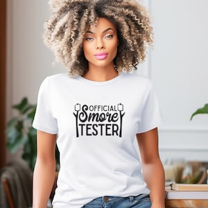 May include: White t-shirt with black text that reads "OFFICIAL Smore TESTER" with a graphic of a marshmallow on a stick.