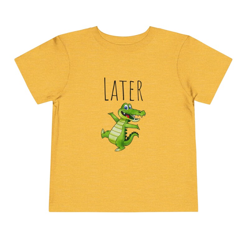 K&ouml;nnte beinhalten: Ein gelbes T-Shirt mit einem gr&uuml;nen Alligator-Cartoon und dem Wort "LATER" in schwarzem Text.