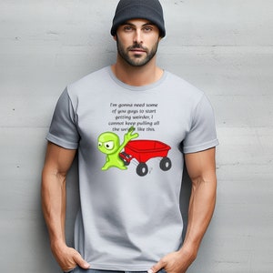 May include: A gray t-shirt with a green alien character pushing a red wagon. The text on the shirt reads: "I'm gonna need some of you guys to start getting weirder, I cannot keep pulling all the weight like this."