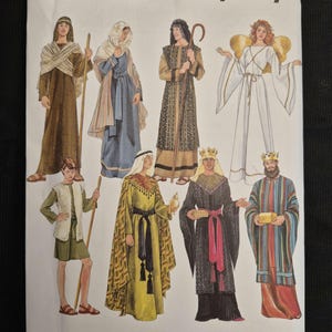Könnte beinhalten: Eine Simplicity Schnittmusterhülle 4795 mit Illustrationen von sieben historischen und religiösen Kostümen, darunter Roben, Tuniken, ein Engel mit Flügeln und Kronen. Der Text enthält den Markennamen Simplicity und den Größenbereich XS-XL.
