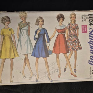 Può includere: Una busta per cartamodello vintage Simplicity, numero 8034, per un abito taglia 12, busto 34. L'illustrazione mostra cinque figure che indossano diversi stili di abito in giallo, bianco, blu, rosso e stampa floreale, con il testo Simplicity 8034.