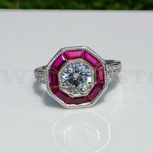 May include: A silver ring with a large, round, clear diamond surrounded by a halo of pink gemstones.