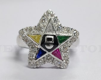May include: A silver ring with a five-pointed star design. The star is set with clear cubic zirconia stones and has a smaller five-pointed star in the center with colored stones. The smaller star has a yellow, green, blue, and red stone.