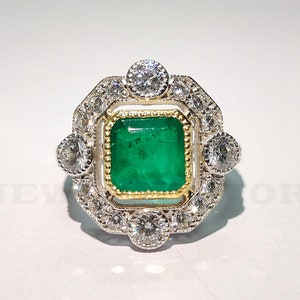 May include: A vintage-style ring with a large emerald green gemstone surrounded by a halo of smaller diamonds. The ring is set in silver and gold.