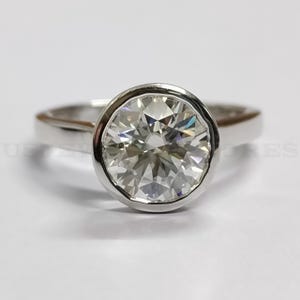 May include: A silver ring with a large, round, bezel-set, clear gemstone.