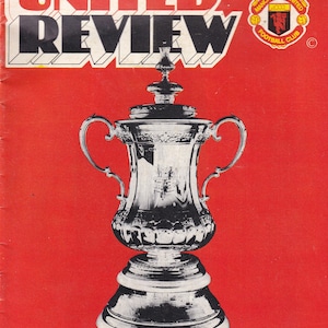 May include: A red vintage United Review magazine cover with a large black and white trophy illustration. The text "UNITED REVIEW" is at the top, with the Manchester United Football Club logo. Below, text reads "MANCHESTER UNITED v TOTTENHAM HOTSPUR", with match details.