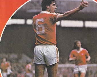 May include: A vintage cover of "United Review" featuring a soccer player in an orange jersey with the number 6. The cover includes the Manchester United logo and text about a match against Nottingham Forest.
