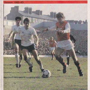 May include: Vintage Arsenal football program cover from the 1982-83 season, featuring a match against Leeds United. The cover has a red and white design with the Arsenal logo and the JVC sponsor. The image shows players in action on the field.