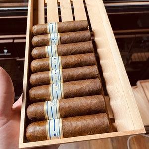 May include: A wooden box filled with ten brown cigars. The cigars have blue and gold labels with the text "CAMPO" and "NO. 1" on them.