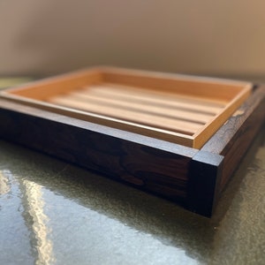 May include: A wooden tray with a dark brown stain and a light wood interior. The tray has a raised edge and is perfect for serving or displaying items.