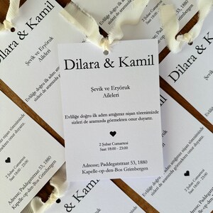 Può includere: Carte di invito di nozze bianche con testo nero che annunciano il fidanzamento di Dilara e Kamil. Le carte includono la data, l'ora e l'indirizzo della festa di fidanzamento. Il testo recita: "Evliliğe doğru ilk adım attığımız nişan törenimizde sizleri de aramızda görmekten onur duyarız." che si traduce in "Siamo onorati di avervi alla nostra festa di fidanzamento, mentre facciamo il nostro primo passo verso il matrimonio."