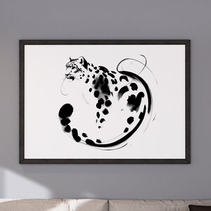 May include: A black and white ink illustration of a snow leopard curled in a circle, framed in a black frame and hanging on a grey wall above a beige sofa.