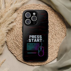 May include: Black smartphone case with a gaming design. The case displays the text "PRESS START" in white, accompanied by a keyboard and mouse graphic in blue and pink. Red and blue lines create a digital effect.