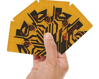 May include: A hand holding a fanned deck of playing cards. The cards have a yellow background with black and red geometric designs and Japanese text. The cards are rectangular with rounded corners.