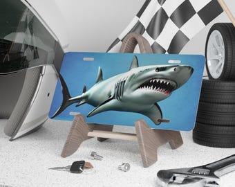 May include: A blue and white license plate featuring a realistic image of a great white shark with its mouth open, showing sharp teeth. The license plate is on a wooden stand.