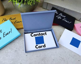 May include: A blue box with a white card inside that says "Contact Card". The card has a blue square on it. The box is open and the card is visible. There are other boxes in the background with the text "The Best Life Ever!" on them.