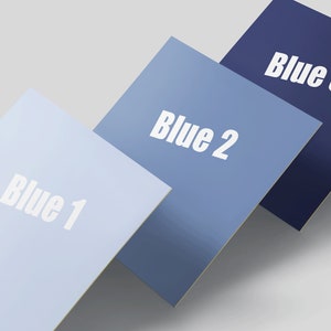 May include: Three square pieces of paper, each a different shade of blue, are stacked on top of each other. The top piece is the darkest blue and says "Blue 3". The middle piece is a lighter blue and says "Blue 2". The bottom piece is the lightest blue and says "Blue 1".