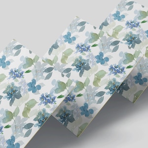 Op de afbeelding: Waterverf bloemenpatroon met blauwe hortensia's en groene bladeren op een witte achtergrond. Het ontwerp wordt herhaald over verschillende rechthoekige vellen, waardoor een gelaagd effect ontstaat. De zachte kleuren en delicate details suggereren een botanisch thema.