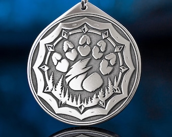 May include: Silver-toned pendant with a detailed paw print design, set within a decorative border. The pendant features a forest scene at the bottom and hangs from a black cord. The design is intricate and the pendant is reflective.