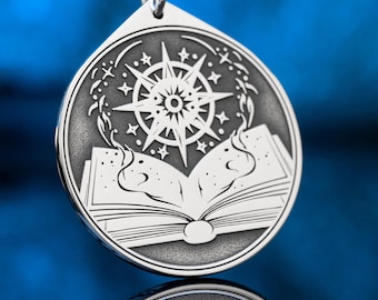 May include: A circular silver-toned metal pendant featuring an engraved design of an open book with swirling magical energy rising from the pages toward a large, multi-pointed starburst symbol. The pendant hangs from a black cord.