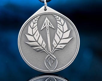 May include: A circular silver-toned pendant featuring an engraved design of a central arrow flanked by two stylized wings. The pendant has a matte finish and is suspended from a black cord, showcasing a detailed metallic texture.