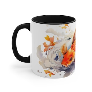 May include: White ceramic coffee mug with a black rim and handle. The mug features a watercolor illustration of two koi fish swimming in a swirling pattern of water and orange flowers.