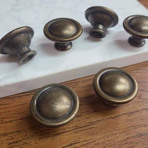 May include: Six antique bronze cabinet knobs with a rounded design. The knobs have a distressed finish and a classic, vintage aesthetic. These knobs are ideal for adding a touch of elegance to furniture or cabinetry.