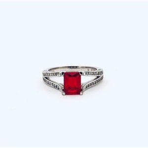 May include: A silver ring with a large, rectangular, bright red gemstone at the center. The band splits into two sections on either side of the gemstone, each lined with small, clear stones. The ring is set against a white background.