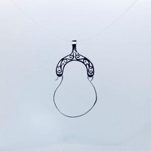 Könnte beinhalten: Ein silberfarbener Anhänger mit offenem Design. Der Anhänger hat eine dekorative gewölbte Oberseite mit wirbelnden Mustern und einen tropfenförmigen unteren Teil. Er hängt an einer dünnen, fast unsichtbaren Schnur und erzeugt einen Schwebeeffekt.