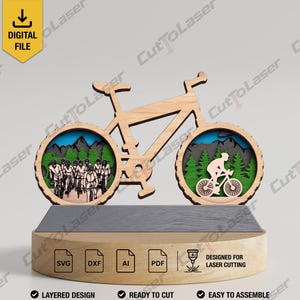 以下が含まれることがあります： 2つの円形の切り抜きがある自転車型の木製レイヤードディスプレイ。左側の車輪にはトレイル上のサイクリストのグループ、右側の車輪には森の中のサイクリストが描かれています。台座にはSVG、DXF、AI、PDFファイルのアイコンが含まれています。