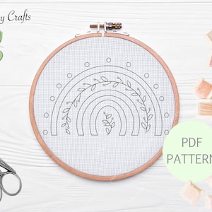 Peut inclure: Un motif de broderie noir et blanc d'un arc-en-ciel avec des feuilles sur un fond blanc. Le motif est dans un cerceau de broderie en bois. Le texte "PDF PATTERN" est sur un cercle vert.