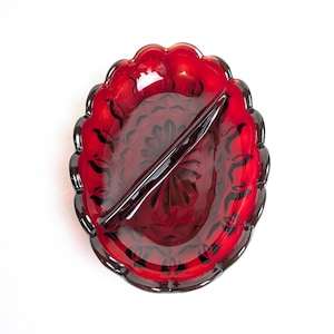 May include: A ruby red glass divided serving dish with a scalloped edge. The dish has a central divider and a floral pattern. The dish is oval-shaped and is on a white background.