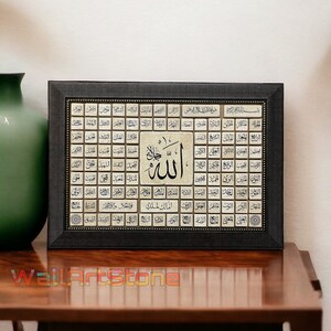 May include: A framed artwork with a black frame and a beige background. The artwork features a grid of Arabic calligraphy with the word "Allah" in the center. The calligraphy is in gold and black.
