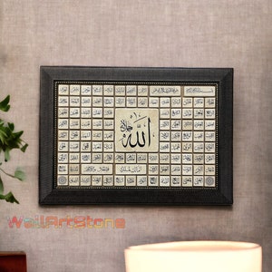 May include: A framed black and gold Islamic art print with the word "Allah" in Arabic script surrounded by 99 names of God in Arabic. The print is on a beige background and has a black frame with gold accents.