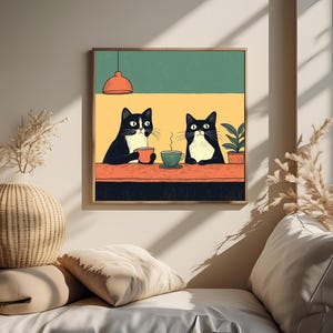 K&ouml;nnte beinhalten: Gerahmter Kunstdruck mit zwei schwarz-wei&szlig;en Katzen an einem Tisch, jede mit einer Tasse Kaffee. Der Hintergrund ist gr&uuml;n und gelb, mit einer roten Pendelleuchte. Eine Topfpflanze ist ebenfalls zu sehen.