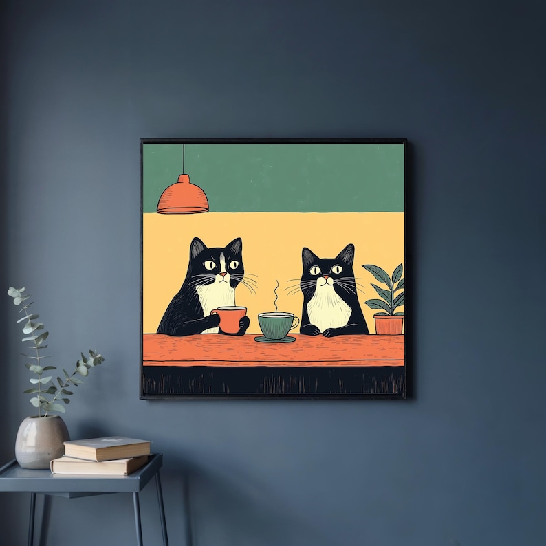 K&ouml;nnte beinhalten: Gerahmter Kunstdruck mit zwei schwarz-wei&szlig;en Katzen, die an einem Tisch sitzen und jeweils eine Tasse halten. Der Hintergrund ist gelb und gr&uuml;n, mit einer kleinen Topfpflanze. Eine rote Pendelleuchte h&auml;ngt dar&uuml;ber.