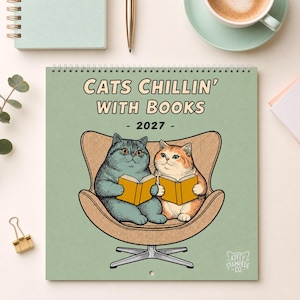 May include: A 2027 wall calendar with a light green cover featuring the text "CATS CHILLIN' WITH BOOKS". The illustration shows a grey cat and an orange tabby cat sitting in a tan armchair, each holding an open yellow book. The logo "KITTY STAMPEDE CO." is in the bottom right corner.