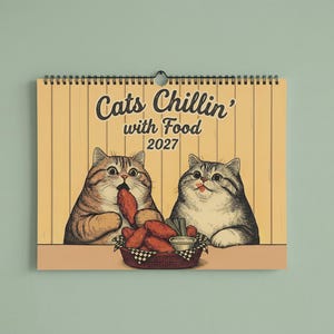 Puede incluir: Un calendario de pared para 2027 con fondo amarillo que muestra dos gatos ilustrados comiendo alitas de pollo de una cesta. El texto dice Cats Chillin' with Food 2027. El calendario est&aacute; encuadernado con una espiral de metal negro en la parte superior.