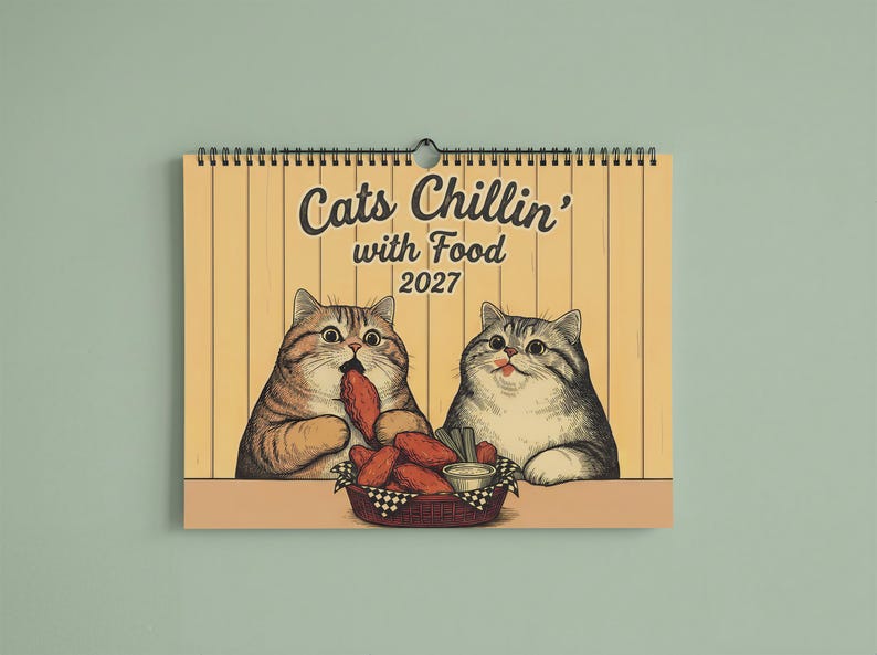 Puede incluir: Un calendario de pared para 2027 con fondo amarillo que muestra dos gatos ilustrados comiendo alitas de pollo de una cesta. El texto dice Cats Chillin' with Food 2027. El calendario est&aacute; encuadernado con una espiral de metal negro en la parte superior.