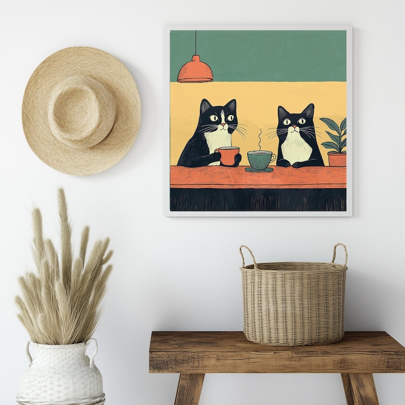 K&ouml;nnte beinhalten: Ein gerahmter Kunstdruck zeigt zwei schwarz-wei&szlig;e Katzen an einem Tisch, die jeweils eine Tasse Kaffee halten. Der Hintergrund weist ein gr&uuml;nes und gelbes Farbschema mit einer orangefarbenen Leuchte auf. Ein Strohhut und eine dekorative Vase mit getrockneten Pflanzen sind ebenfalls zu sehen.