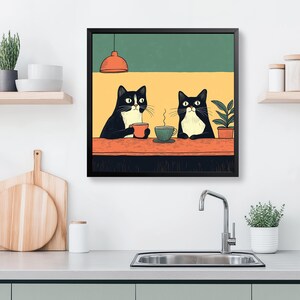 K&ouml;nnte beinhalten: Ein gerahmter Kunstdruck mit zwei schwarz-wei&szlig;en Katzen an einem Tisch, jede mit einer Tasse Kaffee. Der Hintergrund ist gelb und gr&uuml;n, mit einer kleinen Pflanze und einer orangefarbenen Pendelleuchte. Die Katzen scheinen sich zu entspannen.
