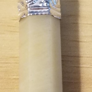 May include: A pendant featuring a light beige, rectangular crystal with a silver-colored metal cap and bail. The top of the pendant has a dark brown, rounded crystal. The pendant is displayed against a light brown wooden surface.