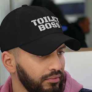 May include: A black baseball cap with white embroidered text that reads "TOILET BOSS".